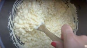 Creamy mac and cheese being stirred in a pot with a wooden spoon.